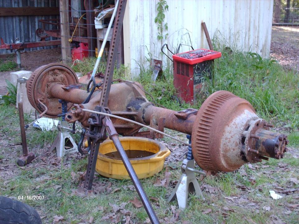 Rusty rear axle assembly on jack stands with a yellow oil pan