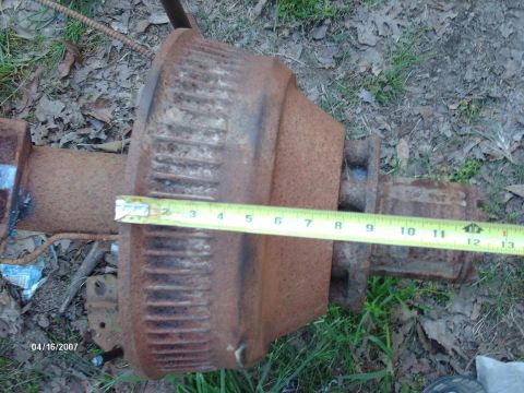 1990 Ford F-150 - A rusty rear axle assembly is measured with a tape measure, indicating its size.