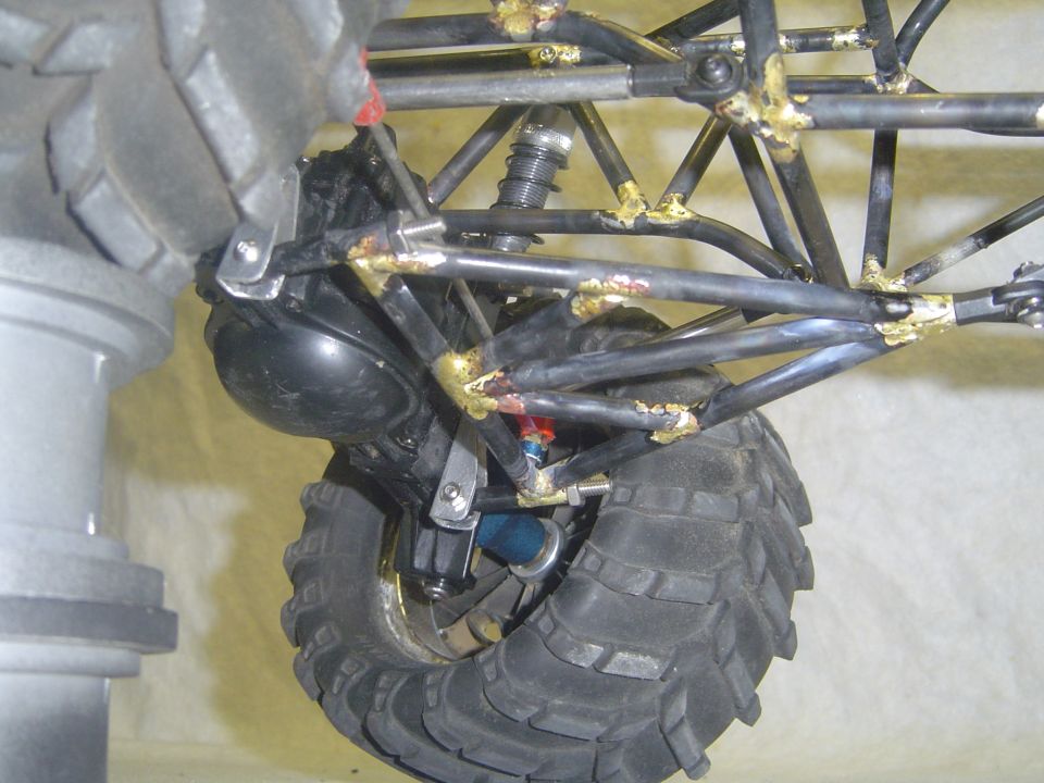 Off-road vehicle's rear suspension and knobby tire, with visible metal tubing and welding
