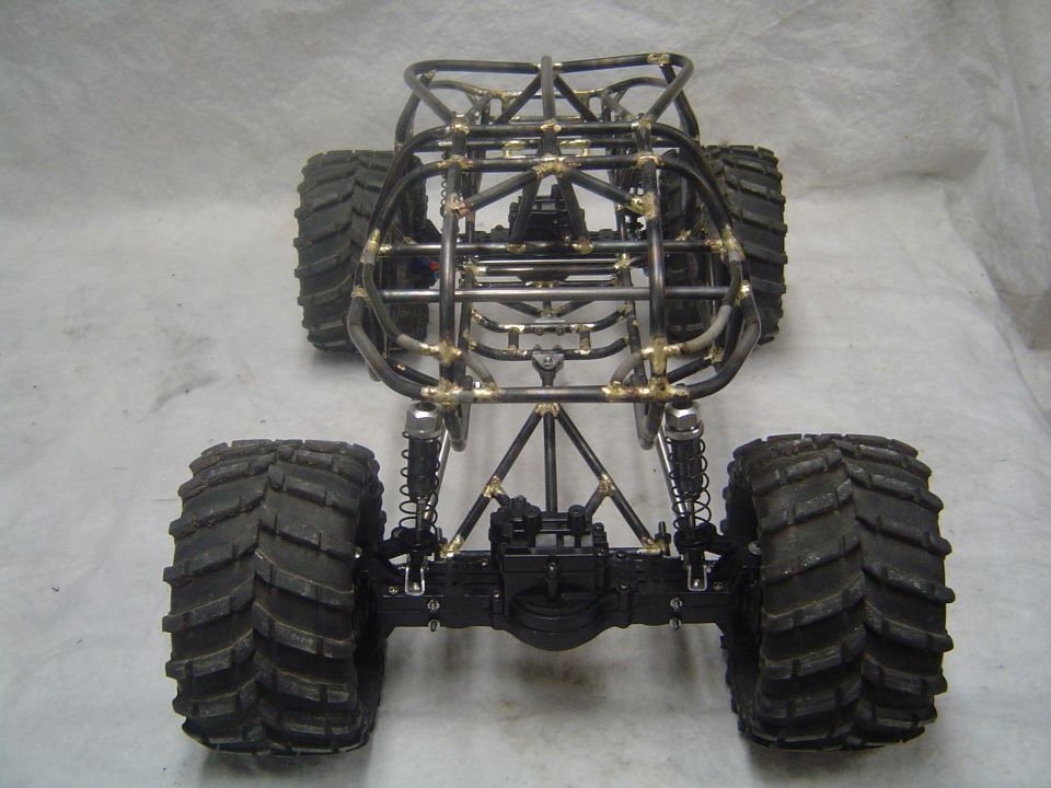 RC rock crawler with a metal tube frame and large off-road tires, viewed from the rear