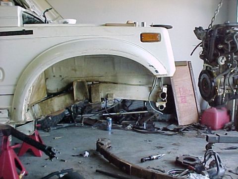 1978 Ford Bronco - The chassis of a white SUV is visible, with the engine removed and parts scattered around the garage floor.
