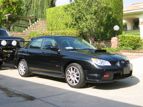 2007 Subaru Impreza - A black Subaru Impreza WRX STI sedan is parked in a driveway next to a dark SUV.