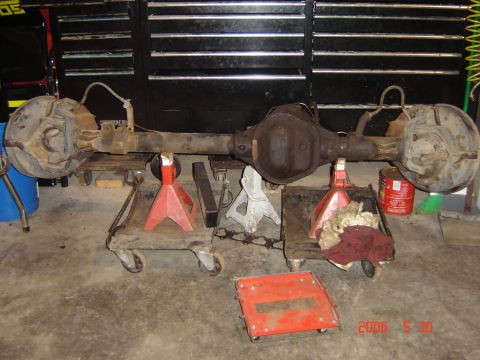 1993 Ford Bronco - A rear axle assembly is supported by jack stands in a garage setting, with tools and equipment around.
