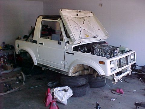 1978 Ford Bronco - A white Suzuki Samurai is undergoing maintenance in a garage, with its hood and engine compartment open.