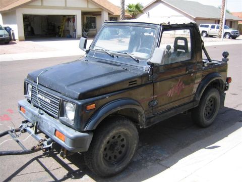 1987 Suzuki Samurai - A black 1987 Suzuki Samurai is parked in a driveway with a trailer hitch attached to the front bumper.