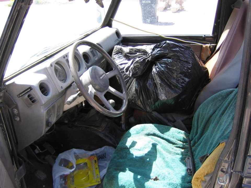 1987 Suzuki Samurai interior with steering wheel, dashboard, and seats covered in blankets and trash bags