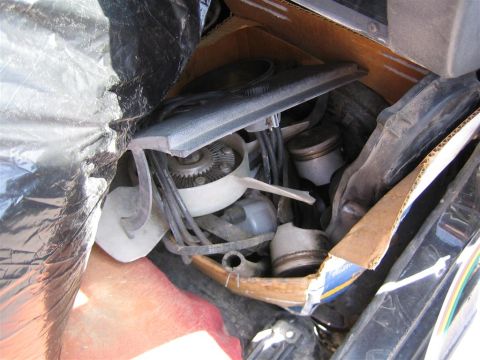 1987 Suzuki Samurai - Engine parts, including pistons and a fan blade, are stored in a cardboard box and covered with black plastic.