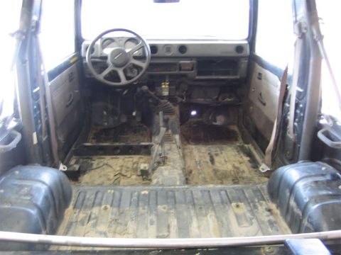 1987 Suzuki Samurai - The interior of this off-road vehicle is stripped down, showing a dirty floor and removed seats, suggesting it is undergoing restoration or…