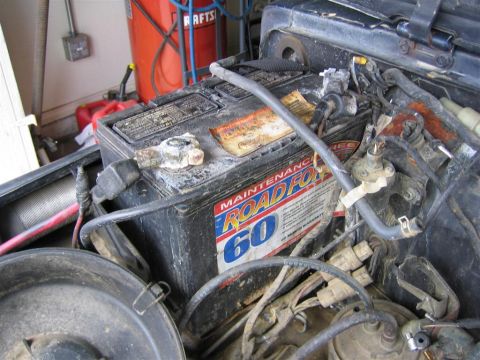 1987 Suzuki Samurai - Close-up of a car battery and surrounding engine components, showing some wear and corrosion.