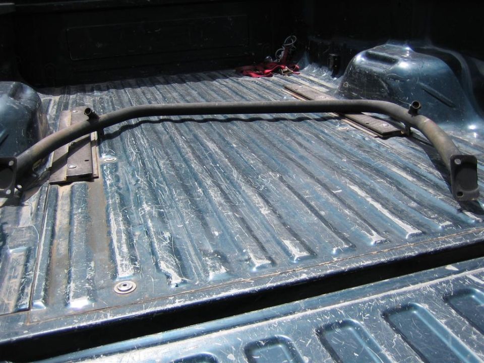 Roll bar in a pickup truck bed, dark metal, curved shape, bolted to bed floor