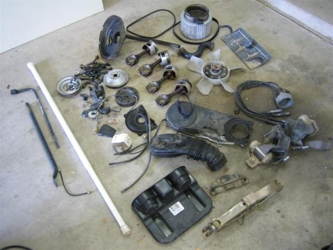 1987 Suzuki Samurai - Disassembled engine and chassis parts laid out on a concrete garage floor, including four piston-and-rod assemblies, a crank pulley, flywhe…