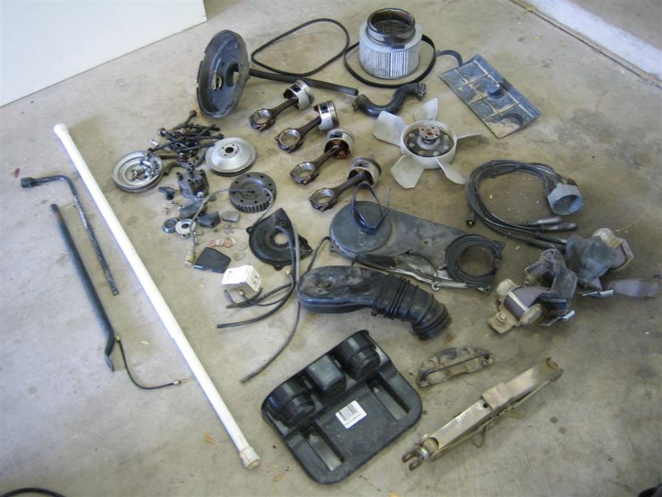 Suzuki engine and chassis parts laid out on garage floor including pistons and fan