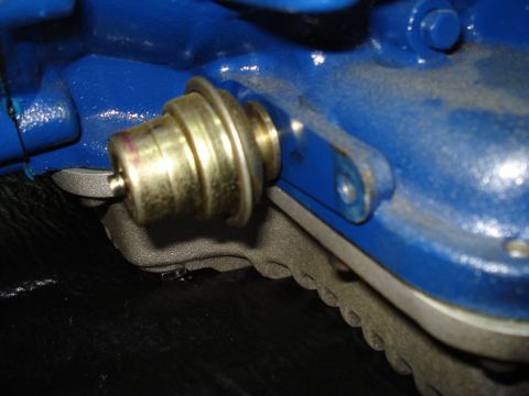 1984 Ford Bronco - A vacuum modulator is shown attached to a blue engine component, with a black surface below.