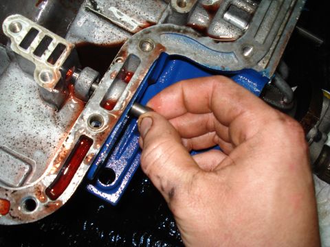 1984 Ford Bronco - Close-up of a hand working on an automatic transmission valve body, with red fluid present.