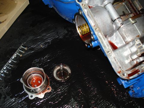 1984 Ford Bronco - Transmission components are laid out on a black surface, showing signs of disassembly and fluid.