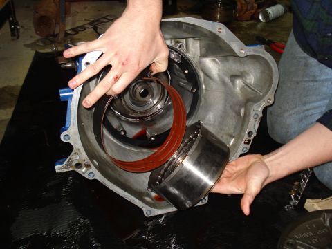 1984 Ford Bronco - Hands holding transmission components during a rebuild, with Supermotors.net logo visible.