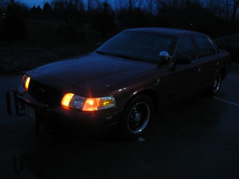 2001 Ford Crown Victoria - A red 2001 Ford Crown Victoria is parked outside at night with its headlights illuminated.
