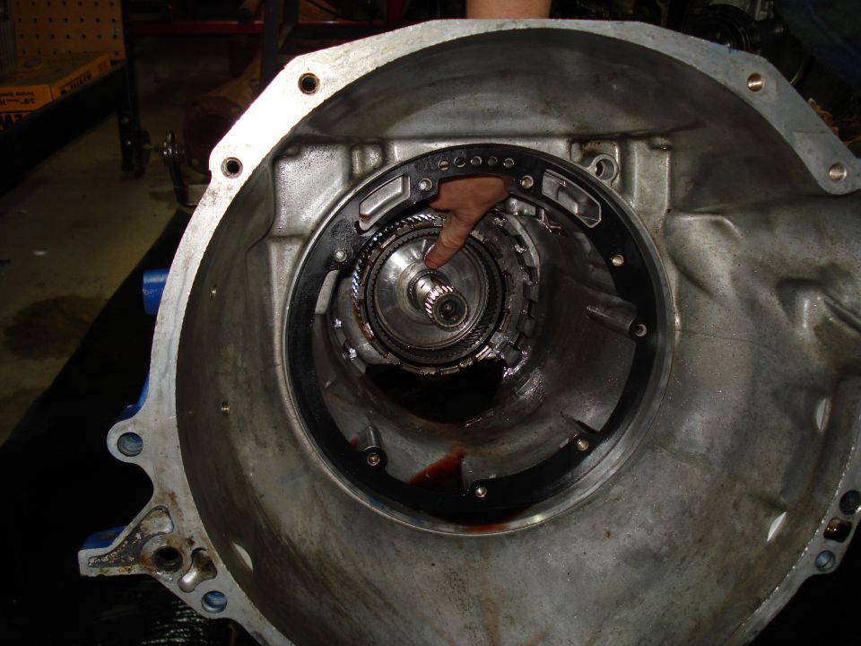 Transmission torque converter with a finger pointing to the splines inside the housing. Red fluid is visible at the bottom