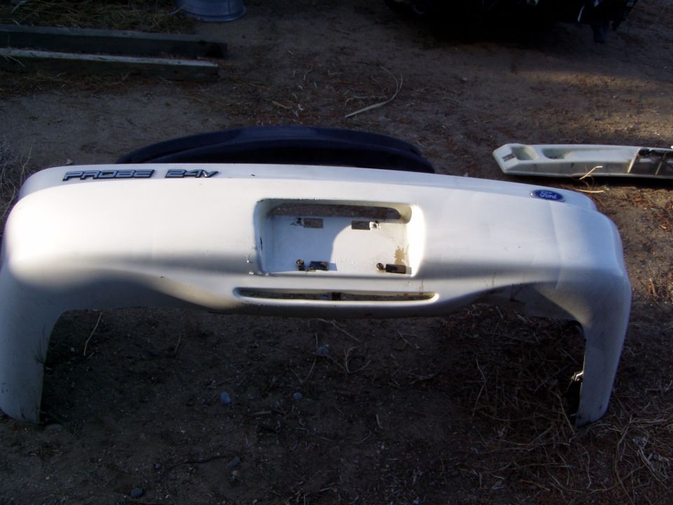 White Ford Probe 24V rear bumper cover lying upside down on dirt with badging visible