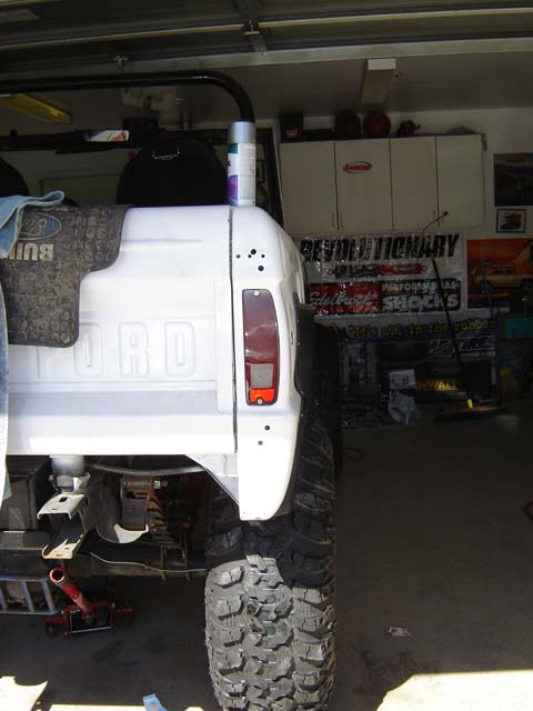 1971 Ford Bronco - The rear quarter panel and large off-road tire of a white 1971 Ford Bronco are visible.
