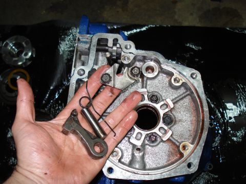 1984 Ford Bronco - A hand holds a lever and spring over a disassembled transmission housing, with a SuperMotors logo visible.