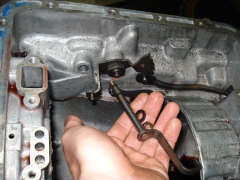 1984 Ford Bronco - A hand is shown holding a metal linkage inside a disassembled automatic transmission pan.