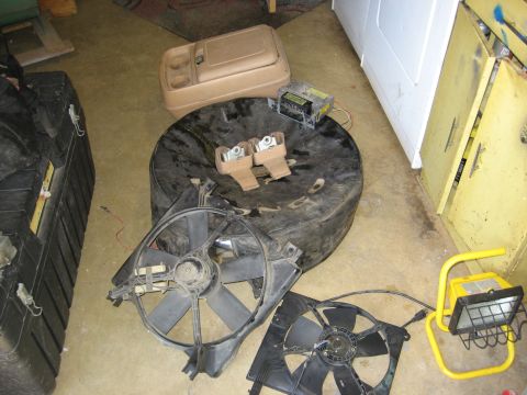 1979 Ford Bronco - Various car parts including a spare tire, radiator fans, and a console storage unit are laid out on the floor.