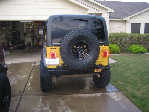 2001 Jeep Wrangler - Rear view of a yellow Jeep Wrangler parked in a driveway with a garage in the background.