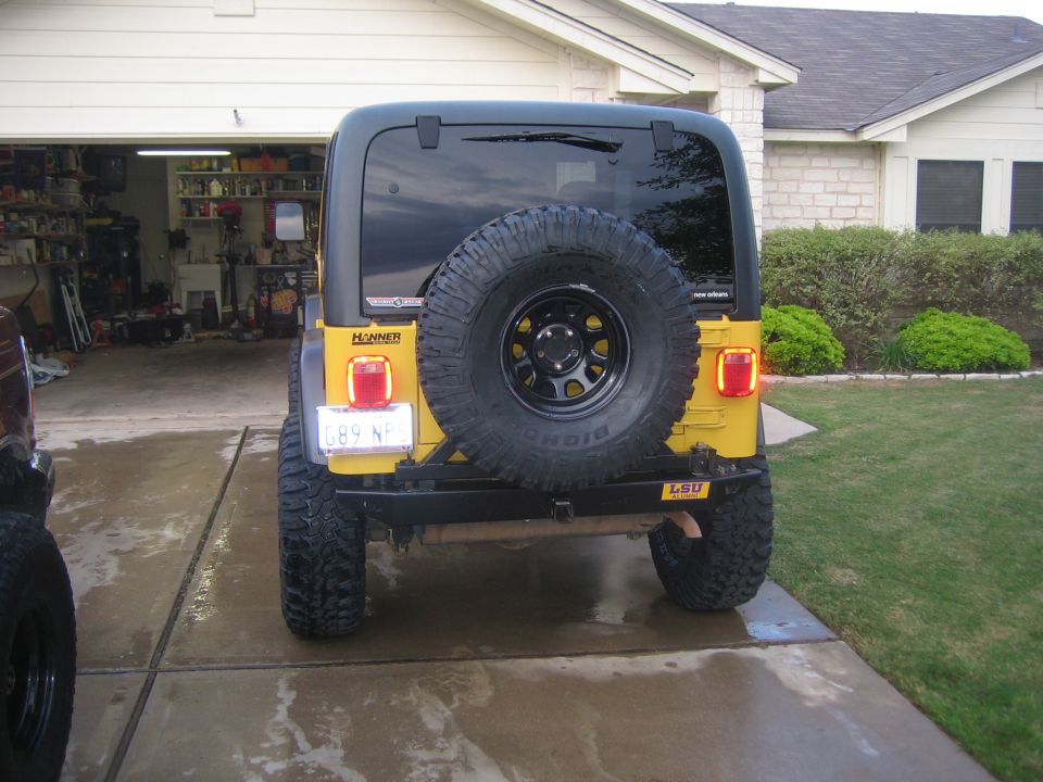 Yellow Jeep Wrangler with a spare tire mounted on the rear, facing away from the camera