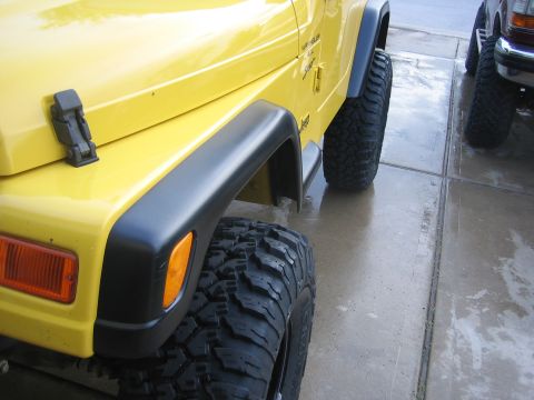 2001 Jeep Wrangler - Close-up view of the front fender and wheel well of a yellow 2001 Jeep Wrangler, parked next to another vehicle.