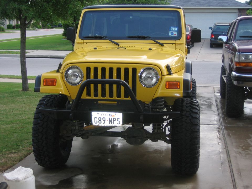 Front view of lifted yellow Jeep Wrangler TJ with tube bumper and mud tires on a driveway