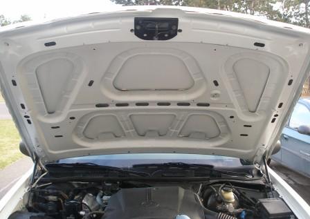 2000 Ford Crown Victoria - The underside of a white car's hood is open, revealing the engine compartment and a portion of another vehicle in the background.