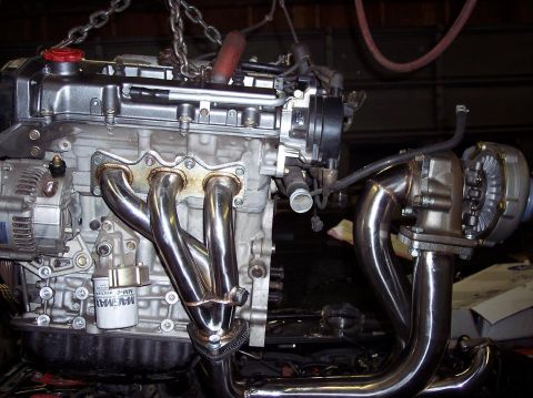 1995 Ford Probe - Engine with turbocharger and exhaust manifold, suspended by chains in a workshop.
