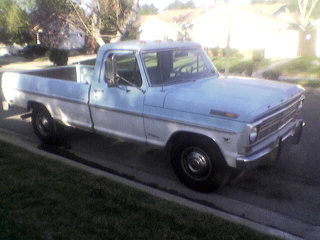 Pale blue late-60s Ford F-250 long bed pickup parked at a suburban curb, front three-quarter