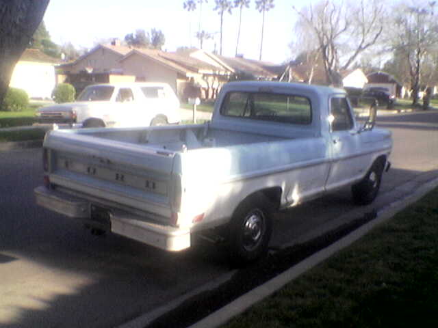 Rear 3/4 view of a light blue and white 1967 Ford F-250 pickup truck parked on a residential street