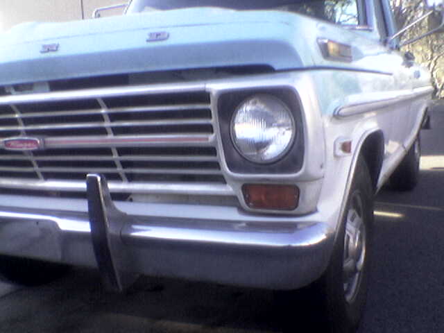 Front corner close-up of a light blue 1960s Ford F-series pickup grille and headlight