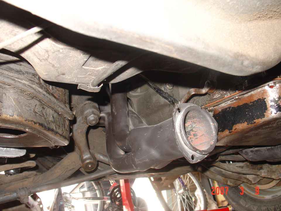 Close-up of black exhaust headers attached to an engine block, viewed from underneath a vehicle