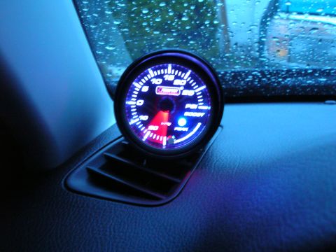1994 Ford Probe - A close-up of a car's interior shows a lit boost gauge and an air vent, with a rain-streaked windshield in the background.