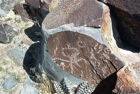 1986 Ford Bronco - Ancient petroglyphs are etched into a large rock formation in a dry, arid landscape.