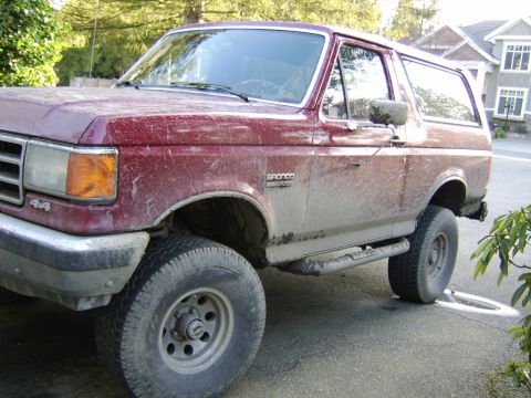 1989 Ford Bronco - This muddy Ford Bronco is parked on a residential street, showing its 4x4 capabilities.