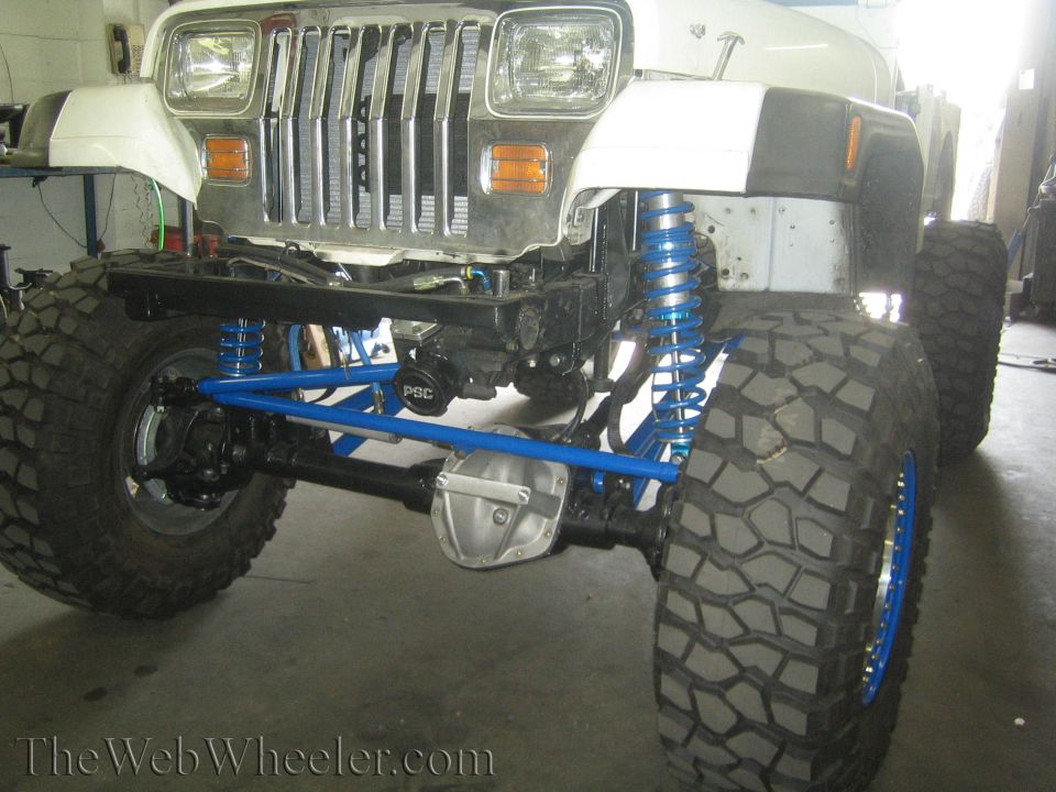 White lifted 4x4 with chrome grille, blue coilovers and beadlock wheels, big mud tires, in a shop