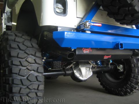1987 Suzuki Samurai - Custom blue rear bumper and dual exhaust system on a heavily modified off-road vehicle with large, aggressive tires.