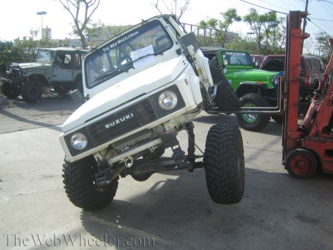 1987 Suzuki Samurai - A heavily modified Suzuki Samurai is being lifted by a forklift, with other off-road vehicles in the background.
