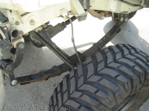1987 Suzuki Samurai - Close-up of off-road vehicle rear suspension, showing leaf springs and a large tire. Text 'OS WR' is visible on the spring.