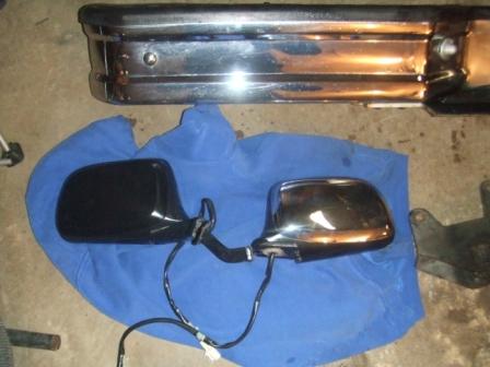 1996 Ford Bronco - A pair of power side mirrors laid on a blue cloth on a garage floor, one with a black painted housing and one with a chrome housing, their…