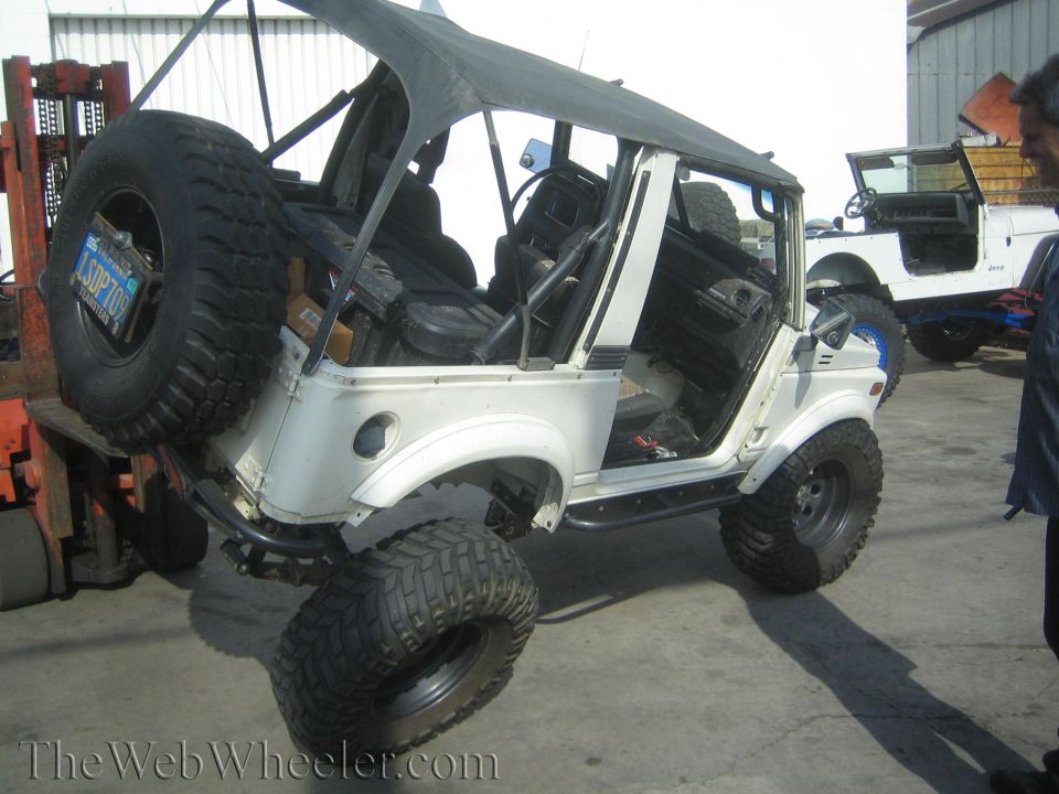 1987 Suzuki Samurai with soft top removed, lifted by forklift, another Jeep visible behind