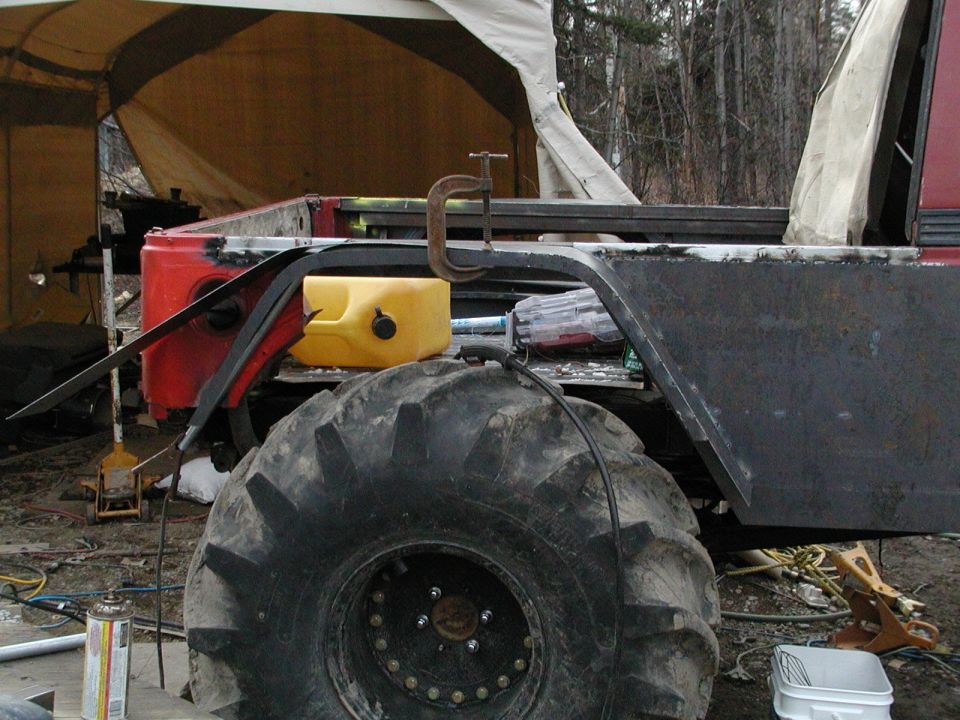 Off-road vehicle bodywork being modified, with large tire and yellow fuel can visible