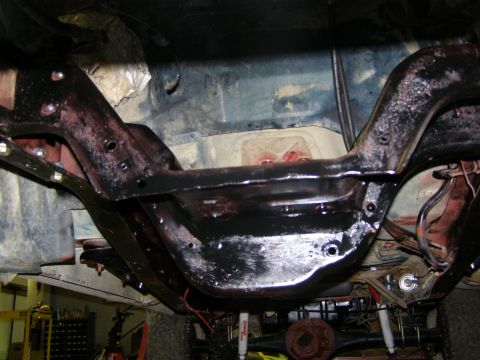 1993 Ford Bronco - The frame and suspension components of a vehicle are visible from underneath, with some red accents on the drivetrain.