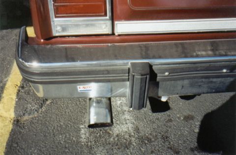 1986 Ford Crown Victoria LTD - The rear of a brown vehicle shows a chrome bumper and an exhaust pipe with an Exxon sticker.