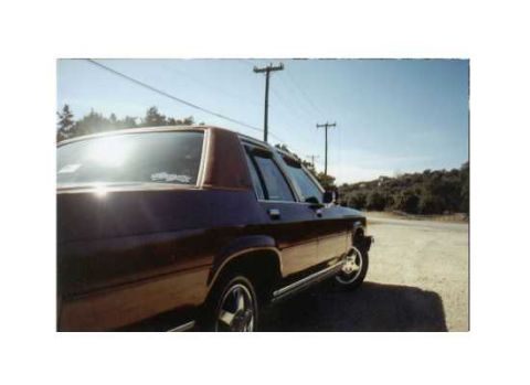 1986 Ford Crown Victoria LTD - A maroon 1986 Ford Crown Victoria LTD is parked on the side of a road under a clear blue sky.